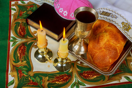 Shabbat candles in glass candlesticks with blurred covered challah background.