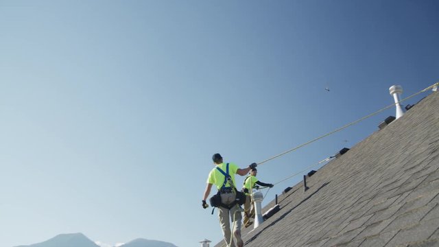 Wide panning low angle shot of workers on roof checking safety lines / Mapleton, Utah, United States