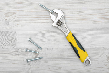 A yellow wrench and four screw bolts placed on light wooden table.