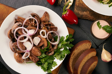 Cooked fried mushrooms on white plate over dark stone background with rye diet bread, low-calorie sauce, fresh red bell pepper and fragrant garlic, top view. Healthy vegetarian food and detox concept