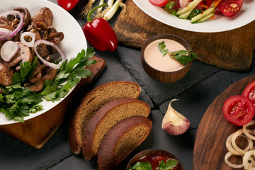 Set of three bowls with different dishes: fried mushrooms, fresh low-calories salad with vegetables and grilled chicken breast. Fresh dietary rye bread and branded sauce on dark stone background