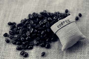 Coffee bean and burlap bag on wooden table blur background dark tone colors