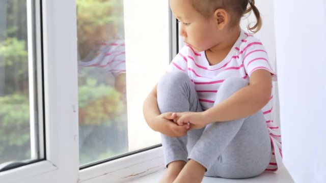 Close up of hands on knees of cute little girl sitting on windowsill of window.