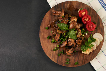 Cooked fried mushrooms on wooden board over dark stone background with copy space, top view. Healthy vegetarian food concept.