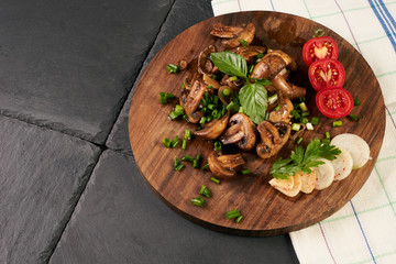 Close-up of a delicious fried mushrooms with baked vegetables in frying pan on wooden round cutting board. Healthy vegetarian food.