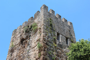 The ancient crenellated tower at the ancient Hadrian's gate in Antalya, Turkey. On the background of blue sky and green trees.
