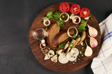 Cold glass of vodka with various traditional russian snack on wooden board over black stone background with copy space. Top view. The concept of national cuisine.
