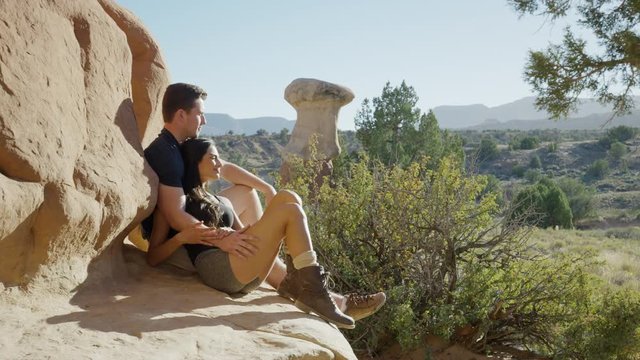 Medium panning shot of couple resting on desert rock / Escalante, Utah, United States