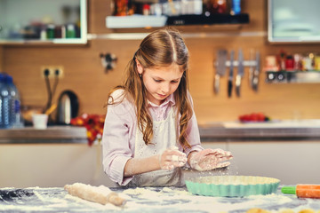 Fototapeta na wymiar Cheerful little girl cooking dough at the kitchen.