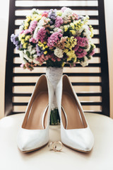 Wedding rings next to the bride's shoes and wedding bouquet