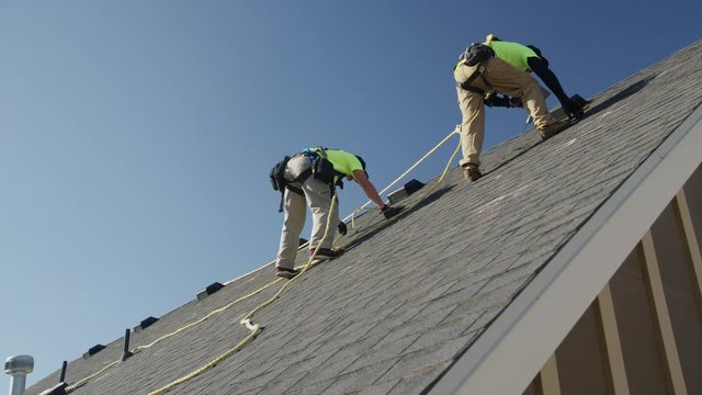 Wide panning low angle shot of workers drilling on roof / Mapleton, Utah, United States