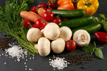 Assortment of fresh colorful vegetables greens and seasoning spices on dark stone background. Healthy food and detox concept. Tasty vegetarian eating.
