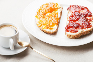 Toast with marmalade next to a cup of coffee on a tablecloth.