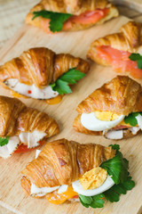 Vertical photo of mini croissants with egg, chicken ham, cheese, tomato, parsley and salmon on wooden board