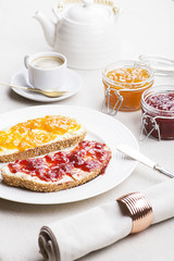Two toasts with strawberry jam and peach next to cup of coffee on tablecloth. Vertical studio shot.