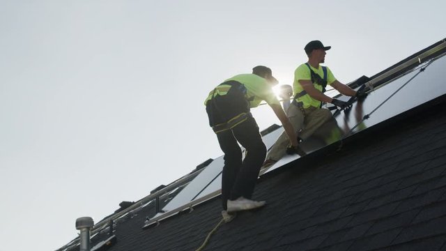 Medium panning low angle shot of workers installing solar panel on roof / Mapleton, Utah, United States