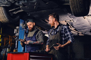 Two mechanics working under the car in a garage.