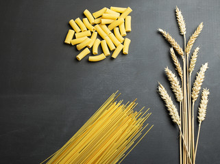 Wheat flower next to pasta on black background.