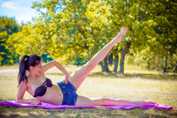 Woman relaxing and does gymnastics on outdoors in city park. Pretty girl with tattoo and good mood at sunny morning 