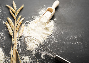 Wheat background next to blender and wooden spoon with flour on black background. Cookware.