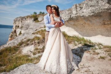 Gorgeous wedding couple posing next to the cave with breathtaking view of lake in the background.