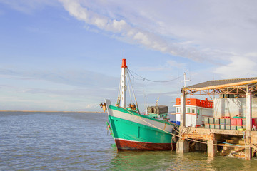 The green fishing boat is whitewashed against the pier with blue sky.