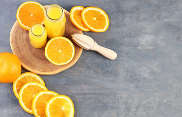 Bottles with orange juice and juicer on grey wooden table