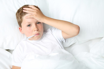 Sick boy with thermometer lying in white bed