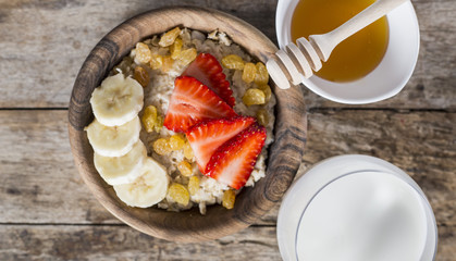 Oatmeal with banana, strawberry and glass of milk on brown wooden table