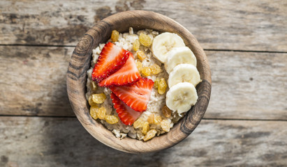 Oatmeal with banana, strawberry and glass of milk on brown wooden table