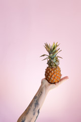 trendy fashion vibrant pineapple on hand, colorful background, summer healthy food theme