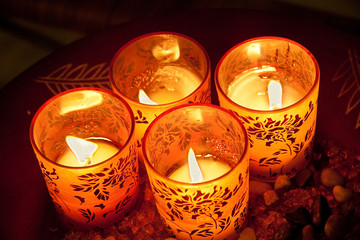 Lit candles in decorated glasses on plate viewed from above