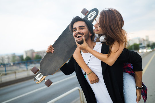 Picture of young attractive couple carrying skateboards