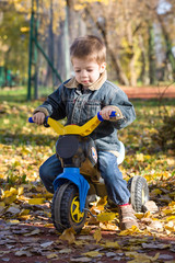 child boy ride a toy motorcycle in a park in autumn