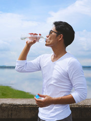 Healthy man with sweat on face and body drinking water after running or exercise on sunny day, thirsty man take a break from outdoor training. Sports, fitness, healthy concepts.