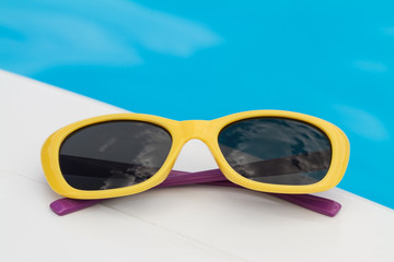 Children sunglasses lying on a deck-chair on blue water background