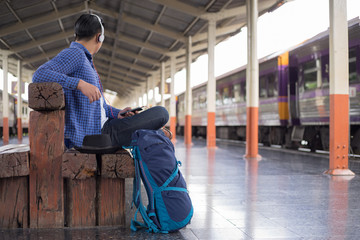 man traveler with backpacker listening to music at trainstation