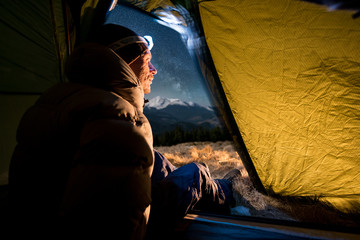 View from inside a tent on the male hiker have a rest in his camping at night. Man with a headlamp sitting in the tent near campfire © anatoliy_gleb