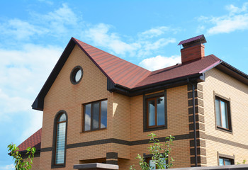 Brick house with attic window rain gutter system and red asphalt shingles roof.