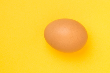 Single brown chicken egg on yellow background