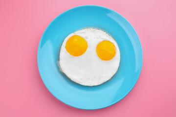 Plate with delicious sunny side up eggs on colour background