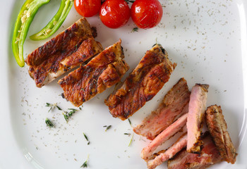 Yummy grilled sliced spare ribs with cherry tomatoes on square white plate, top view