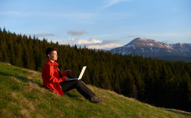 Naklejka na ściany i meble Shot of a cheerful young female working on her laptop resting on top of the mountain on sunset after hiking copyspace nature achievement project education travelling.