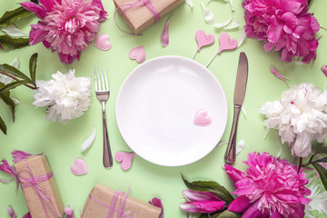 Fototapeta na wymiar Festive table setting with cutlery, peonies and gift boxes on green table.