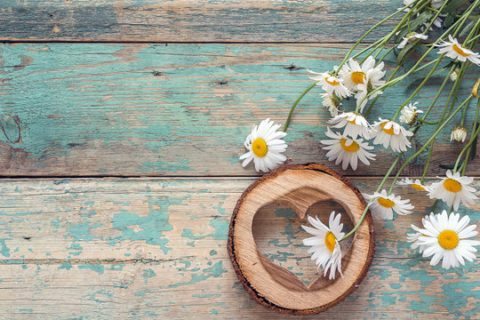 Bouquet of daisies with wooden heart on old wooden background. Place for text.