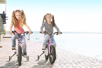 Fototapeta premium Cute little girls riding bicycles near river on sunny day