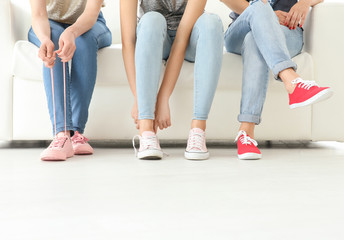 Fototapeta na wymiar Young women with beautiful legs in jeans and sneakers sitting on sofa