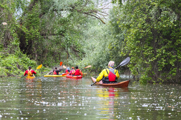Group of people (friends) kayaking in wild river among thickets of plants on biosphere reserve in spring