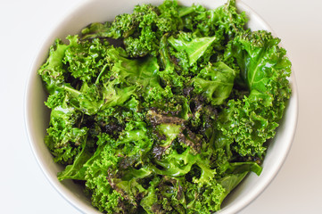 Kale salad in big bowl on white table. Fresh oily kale leaves. Healthy food