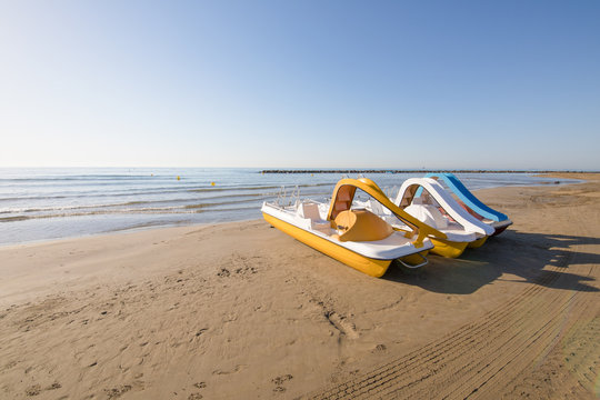 three pedal boats in row on the beach Els Terrers, in Benicassim, Castellon, Valencia, Spain, Europe. Blue clear sky and Mediterranean Sea
